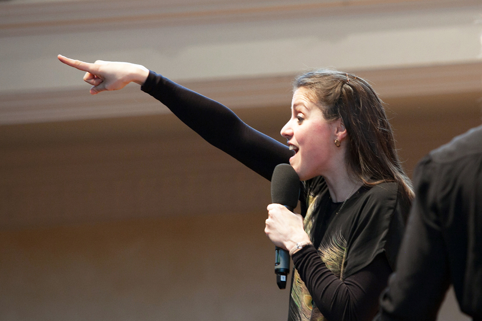 A female student speaking into a speaker, pointing out into the audience.